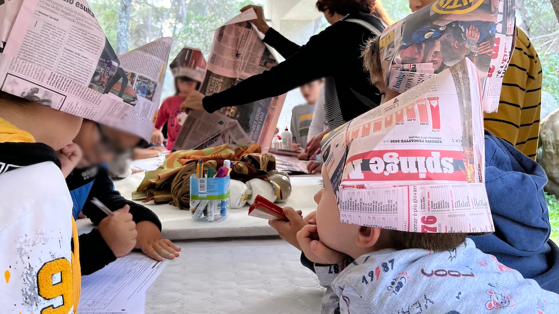 bambini giocano durante un laboratorio con dei cappelli fatti con pagine di quotidiani